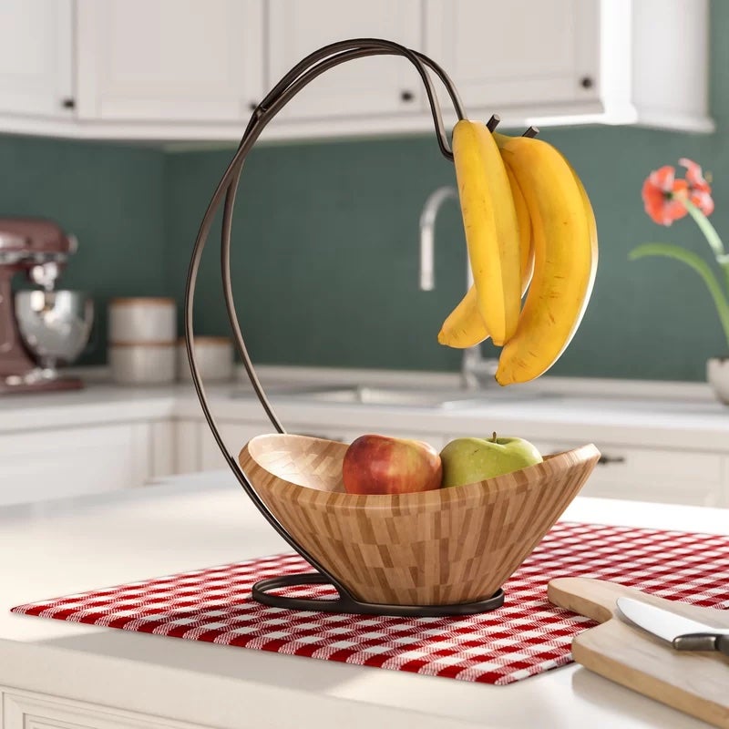 A brown fruit bowl filled with apples and with bananas hanging 