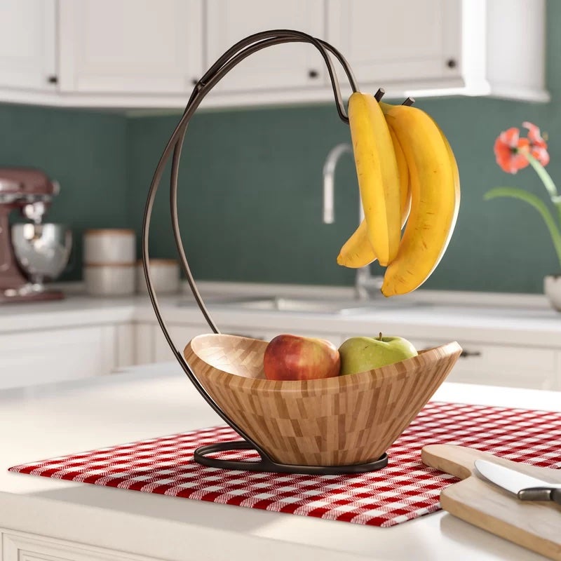 A brown fruit bowl filled with apples and with bananas hanging