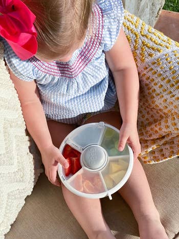 reviewer's kid holding snack spinner with snacks successful it