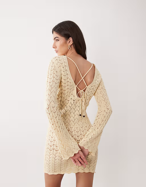Person wearing a patterned crochet formal  with an unfastened  backmost  and crisscross straps, posing with hands down  back
