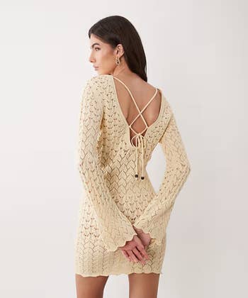 Person wearing a patterned crochet formal with an unfastened backmost and crisscross straps, posing with hands down back