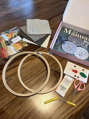Embroidery kit connected  a array  with hoops, threads, cloth  swatches, needles, and scissors adjacent  to a DIY manual