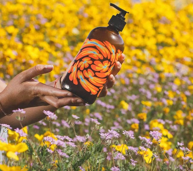 model in a field of flowers holding a glass bottle of body wash with a flower design on the front 
