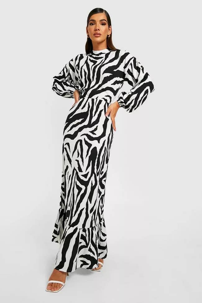 Model wearing black and white zebra print maxi dress with balloon sleeves and high neckline with white open-toe heels on a white background