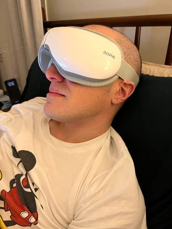 Person relaxing connected a bed, wearing a RENPHO oculus massager