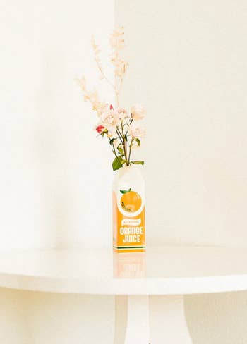 White and orange vintage juice caton-inspired flower vase with flowers inside on top of white table