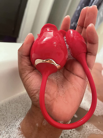 Reviewer holding red rose dual-stimulating vibrator in bathtub