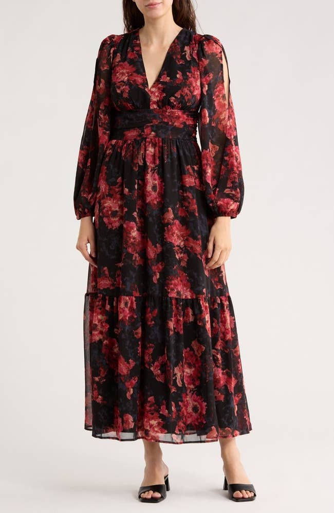 Person wearing a long, floral print dress with a deep V-neck and sheer sleeves, suitable for elegant occasions