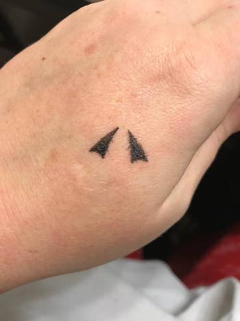 Tattoo of two filled triangle shapes on a person's hand, displayed close-up with blurred background