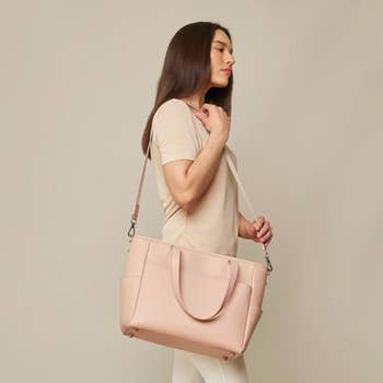 A model posing with a pink tote bag with a long shoulder strap