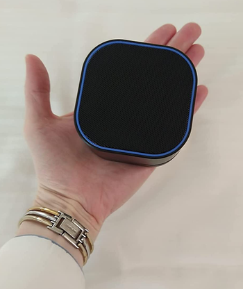 reviewer holding the small black noise machine in the palm of their hand to show scale