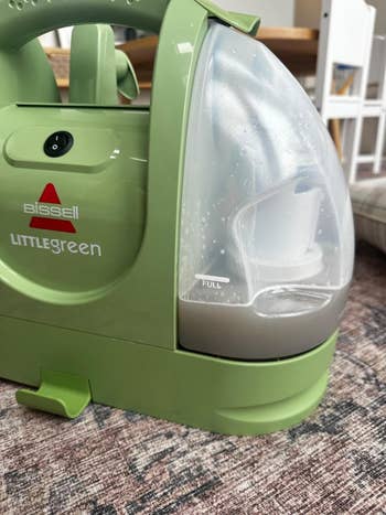 Bissell Little Green portable carpet cleaner with a full dirty water tank on a carpeted floor