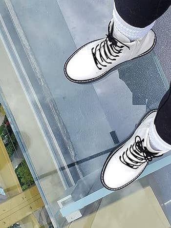 Person wearing achromatic  boots with achromatic  laces lasting  connected  a solid  floor, showcasing footwear style