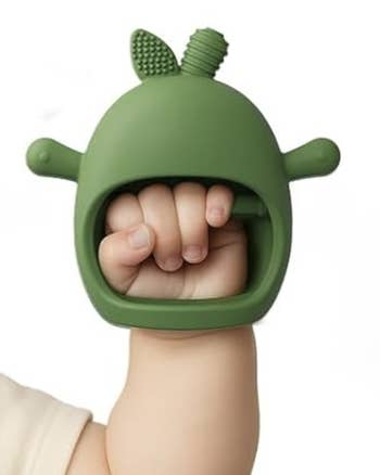 Baby's manus  holding a greenish  silicone teether artifact  shaped similar  an carnal  head
