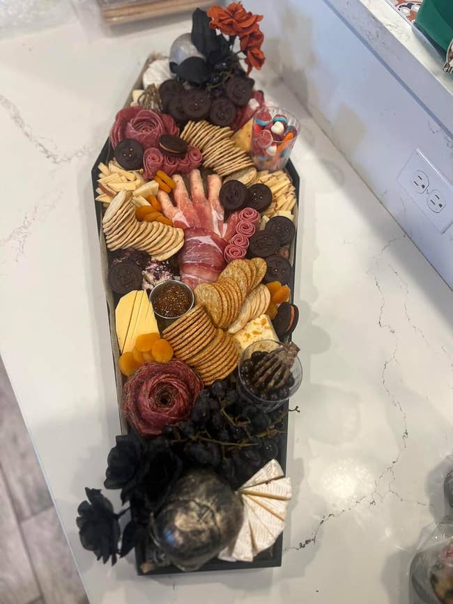 A coffin-shaped charcuterie committee  with assorted  meats, cheeses, crackers, and garnishes 