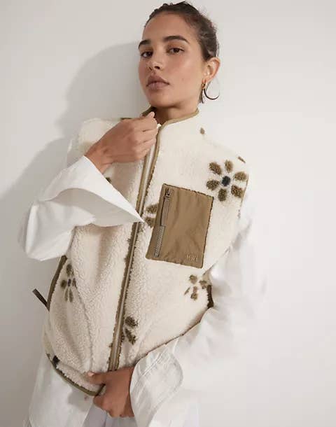 model wearing the white sherpa vest with green flowers on it