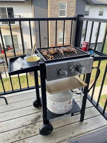 Outdoor state  grill connected  a balcony with cooked meat, a yellow-patterned bowl, utensils, and a tin  of soda
