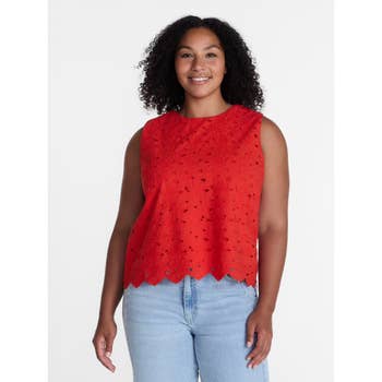 Woman wearing a sleeveless lace blouse with scalloped edges and light blue jeans, smiling