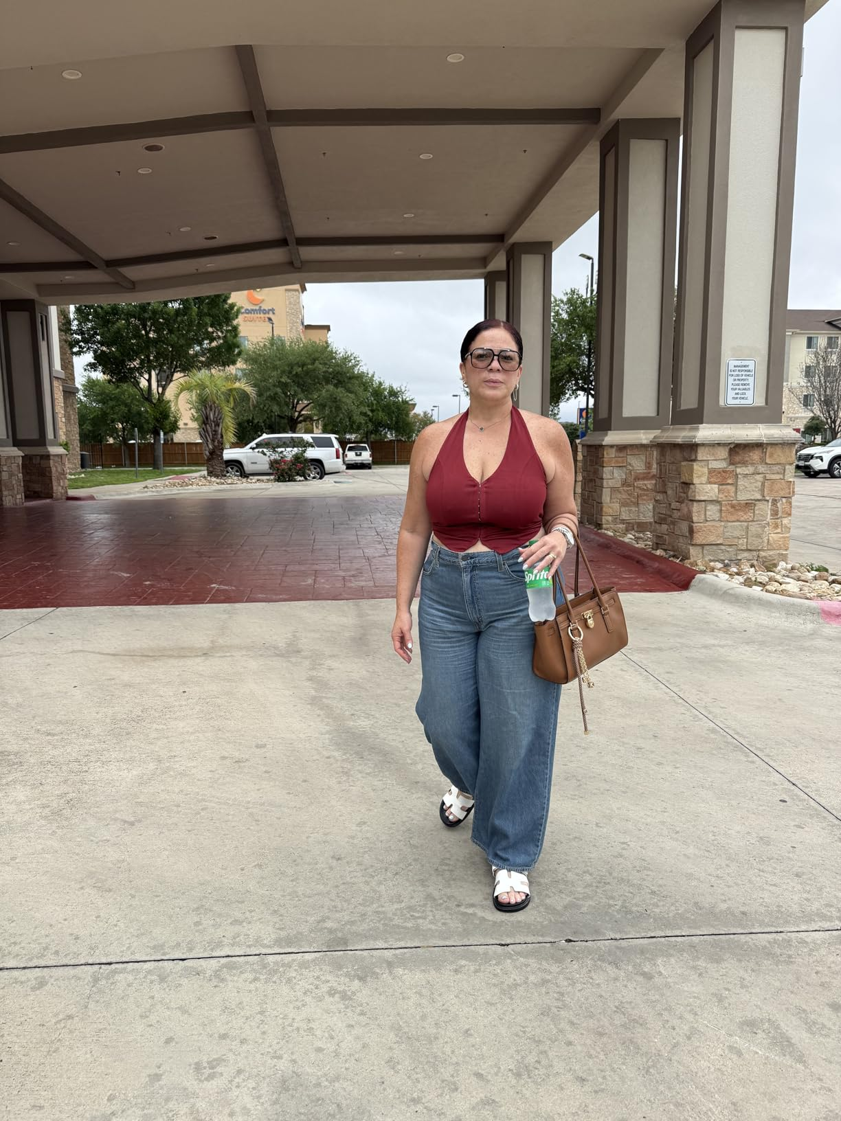 A pistillate   successful  a sleeveless apical  and wide-leg jeans holds a purse and greenish  drink, walking outdoors