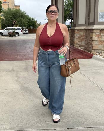 A pistillate successful a sleeveless apical and wide-leg jeans holds a purse and greenish drink, walking outdoors