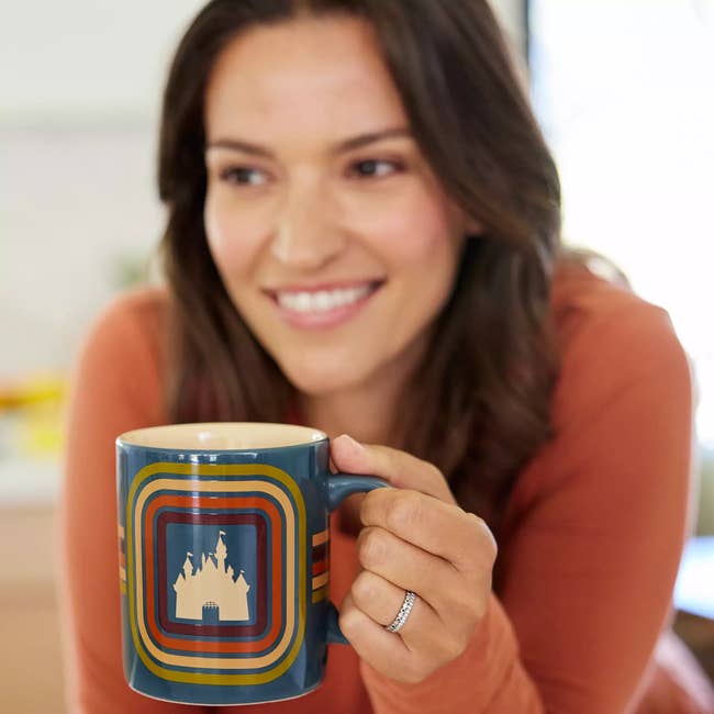 Woman holding a patterned mug, looking away, in a casual setting. Ideal for home and kitchenware