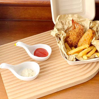 Fried shrimp, chicken, and fries in a container on a wooden tray, with two sauce dishes containing ketchup and tartar sauce