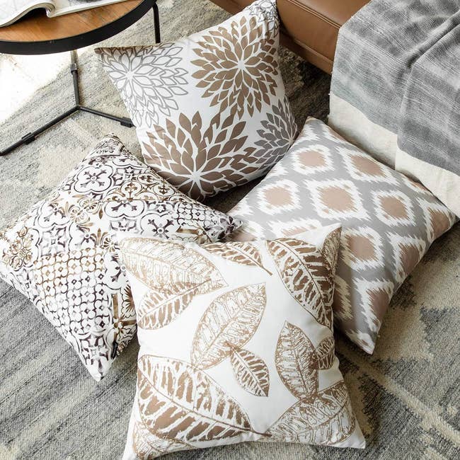 four pillows in white with grey and brown ikat, floral, leaf, and trellis prints on them, respectively