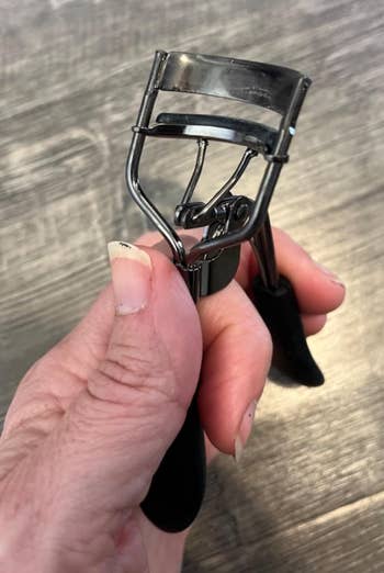 Person holding an eyelash curler with achromatic  handles, showcasing its mechanics  and design
