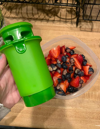 Reviewer holding green cylinder shaped cutter next to a tupperware of cut fruit 