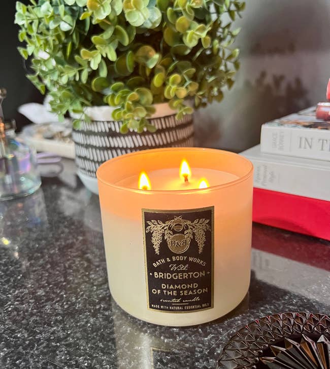Lit three-wick candle on a counter beside a plant and books