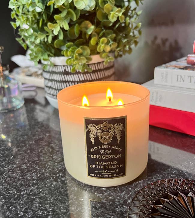 Lit three-wick candle on a counter beside a plant and books