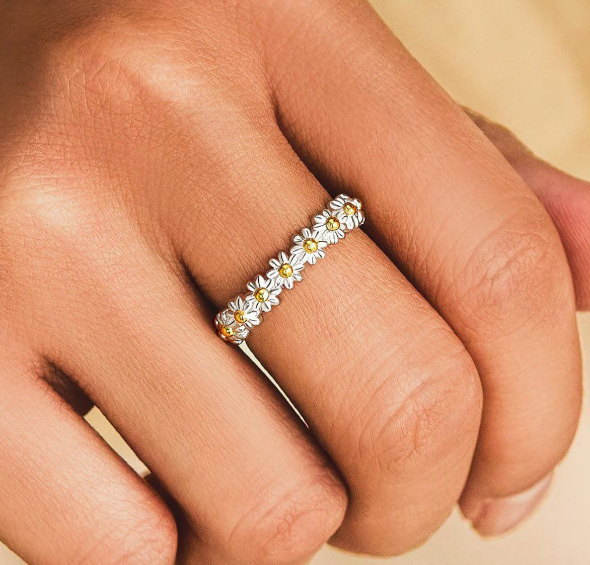 Model is wearing a small silver ring band of daisies on their middle finger