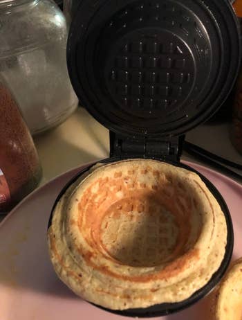 A small waffle bowl cooked into a compact black waffle bowl maker 