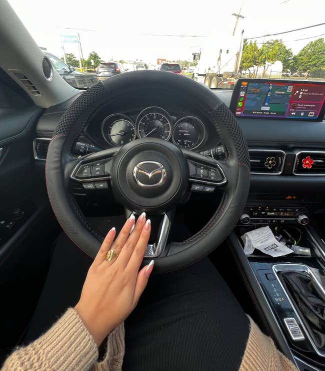 Hand with manicured nails connected a car steering wheel