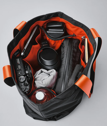 The inside of the tote bag lined with orange fabric with items inside