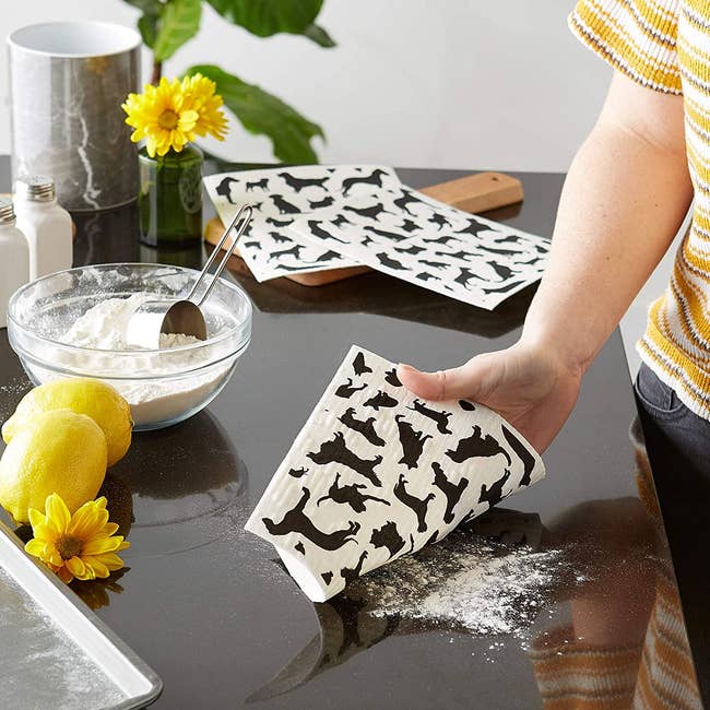A person washing a knife and fork with a square-shaped Swedish dish cloth with dogs printed on it. 