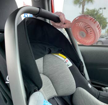 The pink fan with flexible grippers attaching it to a car seat handle 