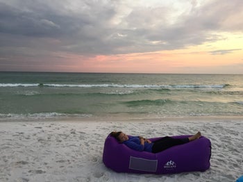 Reviewer's photo showing them lounging on the purple lounge chair at the beach