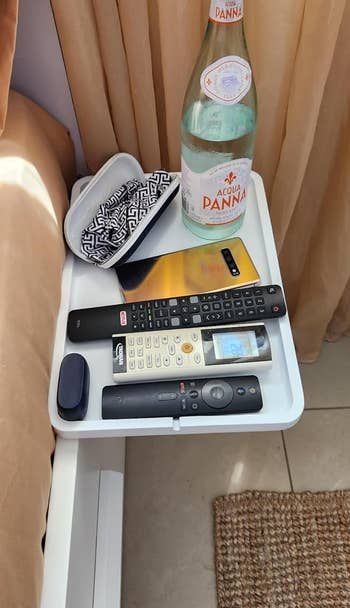 A small table with a water bottle, remote controls, a wallet, and a smartphone