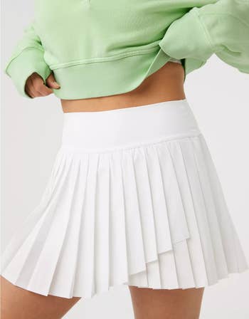 model in green top and white pleated skirt, midsection close-up