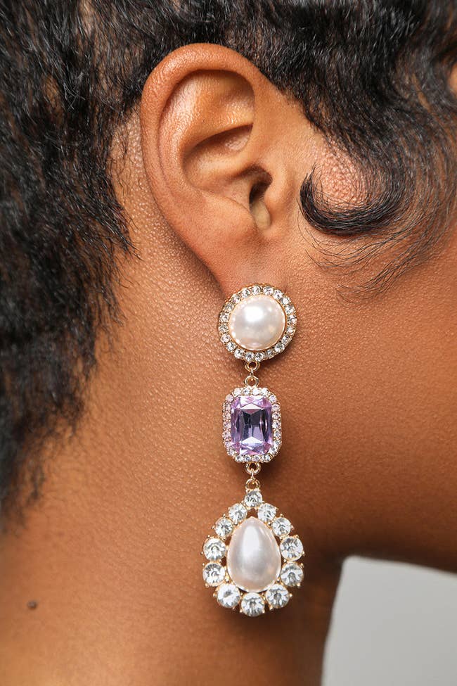 model wearing clear rhinestone trimmed drop earrings with a purple jewel between two large faux pearls