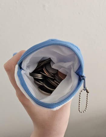 Open zippered coin pouch full of coins, held by a hand