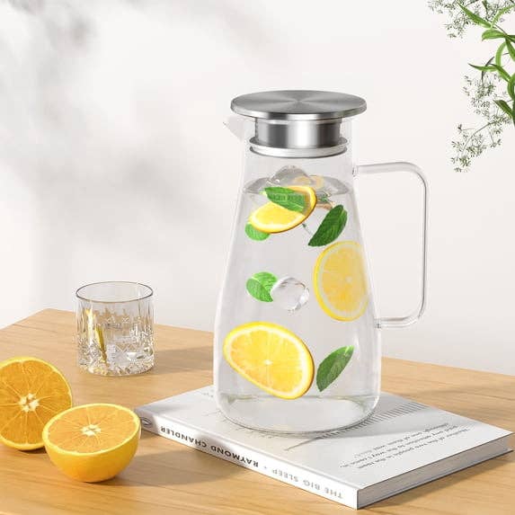 Glass pitcher with citrus slices and mint leaves, sitting connected a book. Nearby, a solid with a citrus portion and halved lemons are visible