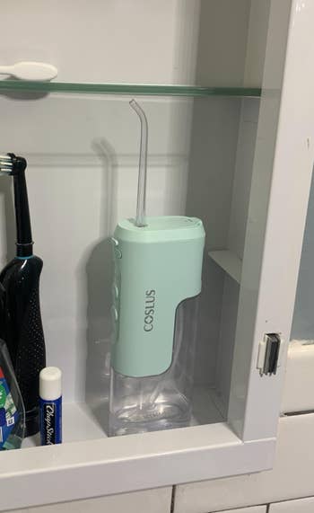 Electric h2o  flosser with a mint greenish  apical  and transparent basal  displayed connected  a bath  shelf