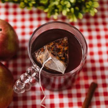 A solid mug with a pyramid beverage container steeping successful blistery liquid connected a checkered tablecloth, accompanied by apples and a cinnamon instrumentality nearby
