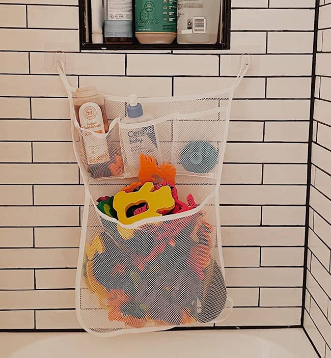 reviewer's photo of a mesh organizer containing bath toys and stuck to the wall