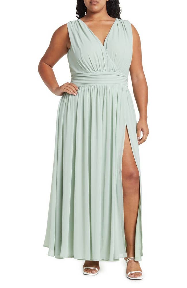 Person wearing a sleeveless, flowing evening gown with a deep V-neck and high slit, paired with strappy heels