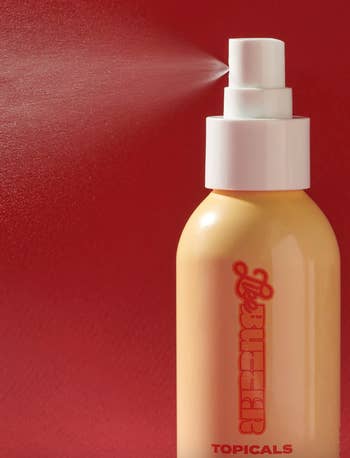 Spray bottle of beauty product on a red background with a mist being dispensed