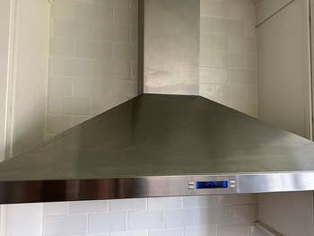 A modern   stainless alloy  room  scope  hood with a integer  show  panel, installed supra  a tiled backsplash