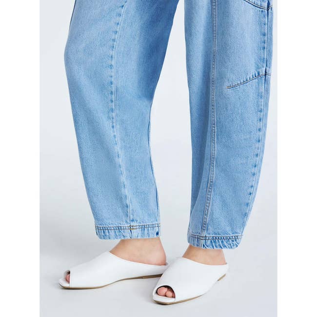 Person wearing loose-fit jeans and white open-toe mules, showcasing casual footwear for shopping
